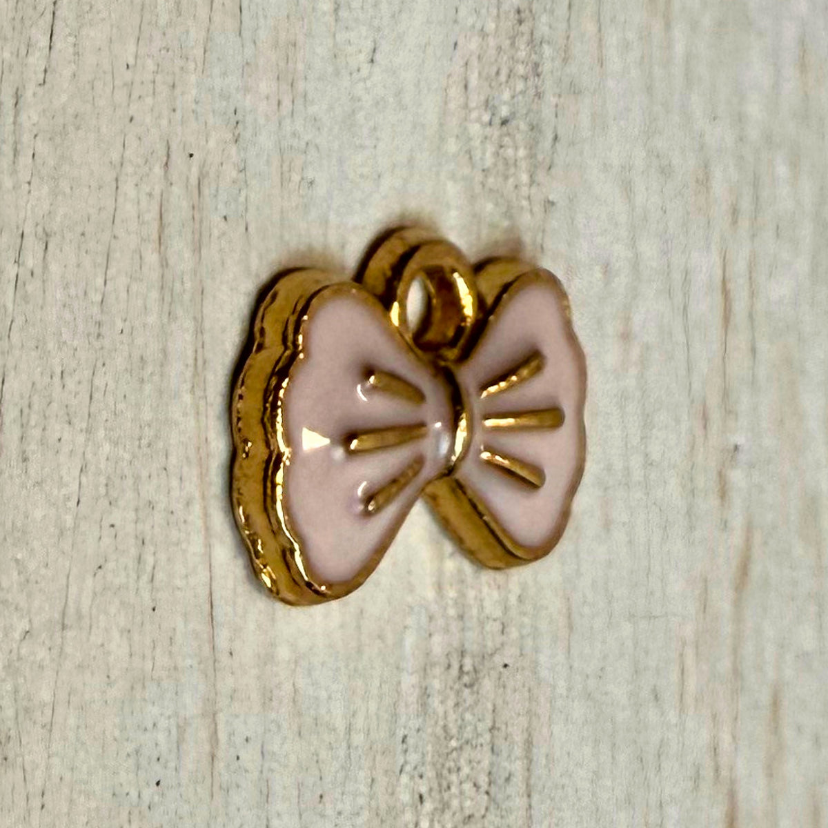 Angled close-up of pink enamel bow western hat charm showing gold-tone edge and depth