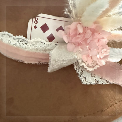Beautified close-up of the exact distressed eight of diamonds card add-on styled behind pink ribbon, lace and florals on a brown western hat