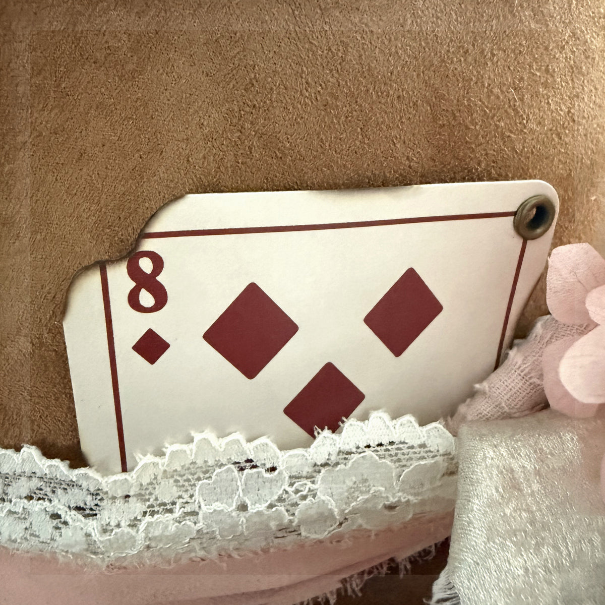 Beautified detail view of the exact distressed eight of diamonds card tucked behind lace and ribbon on a western hat
