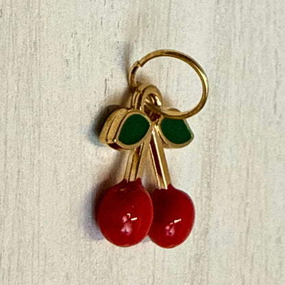 Angled close-up of red enamel cherry charm showing green leaf detail and gold-tone edge