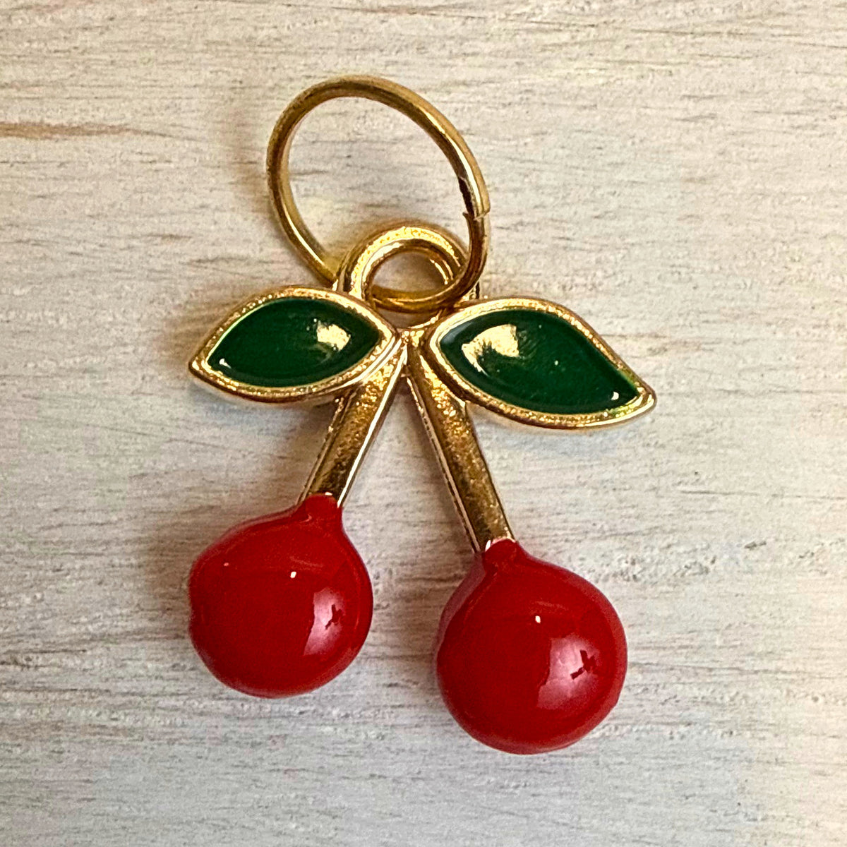 Close-up front view of red enamel cherry charm with green leaves and gold-tone detail