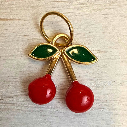 Close-up front view of red enamel cherry charm with green leaves and gold-tone detail